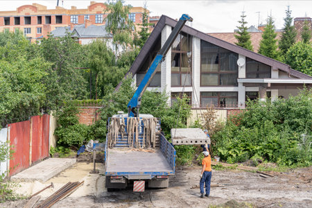 Construction workers unload heavy concrete cement slab from truck with hydraulic telescopic truck...