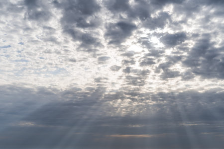 Gloomy sky with real sunbeams in the gap of gray cumulus rain clouds in the afternoon 10-12 hours in the middle latitudes of the sky backgroundの写真素材