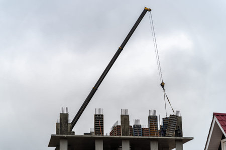 Construction of a new residential monolithic-frame house in the city using a truck crane in cloudy...