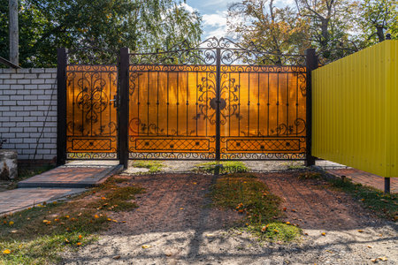 Closed openwork metal gate with orange transparent plastic in the daytime close-up on a private land plot interior view with shadowの写真素材