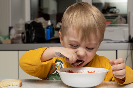 Little blond boy 3 years old is eating soup and bread in the kitchen at the table and close-upの写真素材