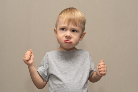 Cute boy in gray t-shirt blond age 3 years isolated on gray background shows anger and rage, points...