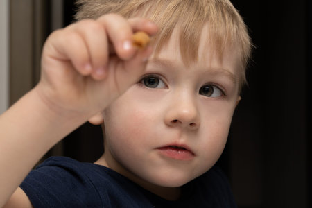 Little boy 3 years old blond white eating a waffle tube on a black background, copy space.