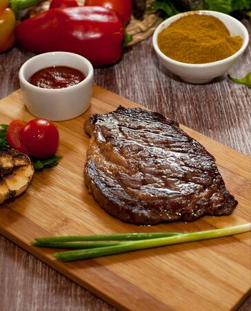 large steak on a wooden board next to fresh vegetables sauce on a wooden backgroundの写真素材