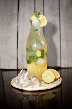Homemade lemonade with berries & lemon ice in a transparent bottle water drops on a wooden stand on a dark backgroundの写真素材