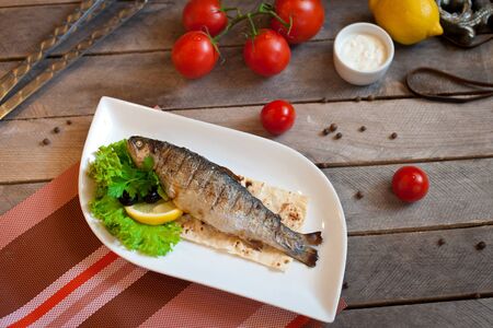 food photo grilled fish trout with vegetables on a white plate with onion halves tomatoes green branches on a blue wooden backgroundの写真素材