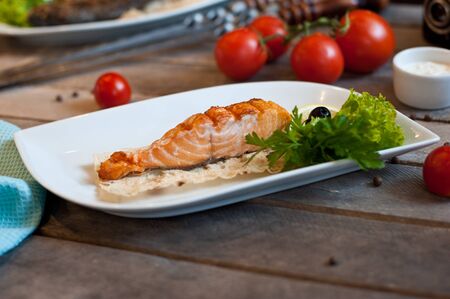 food photo steamed fish with vegetables on a white plate with onion halves tomatoes green branches on a blue wooden backgroundの写真素材
