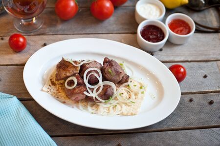 barbecue meat dish on a plate with greens tomatoes and sauce on a wooden backgroundの写真素材