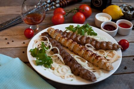 Lula kebab meat dish on a plate with greens tomatoes and sauce on a wooden backgroundの写真素材