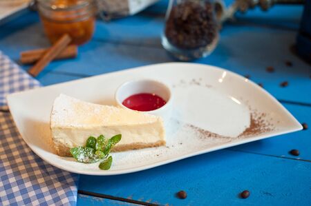 cheesecake on a white plate with a sprig of mint on a blue wooden background raspberry sauce on a white plateの写真素材