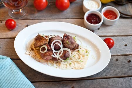 Meat kebab with onions on a white plate on a wooden background. Grilled meatの写真素材