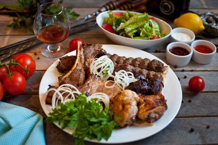 Assorted grilled meat on a white plate with herbs. Lots of meat on a wooden background with sauces and vegetablesの写真素材