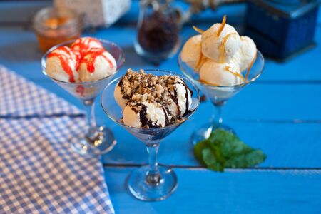 Vanilla ice cream in glasses with strawberry syrup, chocolate and lemon zest on a blue backgrounの写真素材
