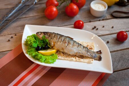 Grilled trout fish with spices, herbs and lemon fried on a grill on a white plate, top viewの写真素材