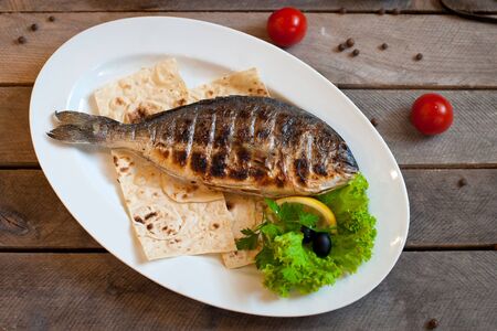 Fried fish Dorada, sea bream with spices, herbs and lemon fried on a grill on a white plate, top viewの写真素材