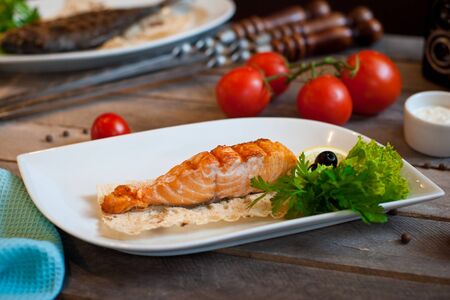 Grilled salmon steak served on a white plate with lemon and herbs. wooden backgroundの写真素材