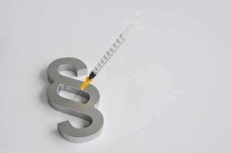 Close up of a hypodermic syringe and a paragraph sign - Symbol for the legal aspects of mandatory vaccinationの写真素材