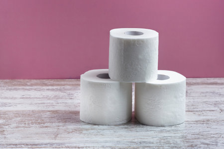 Three rolls of white toilet paper stand in a pyramid on a wooden table on a pink backgroundの写真素材