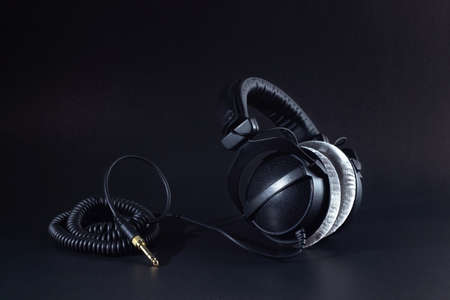 Closed-back studio headphones with a coiled cable stand sideways on a black backgroundの写真素材