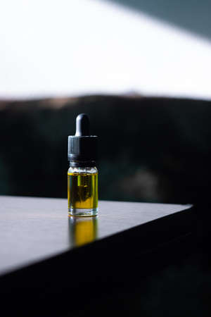 A glass bottle with a pipette filled with cbd oil stands on a dark wood table, against a dark background.の写真素材
