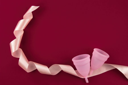 Two eco-friendly, reusable pink colored menstrual cups made of soft medical grade silicone lie...