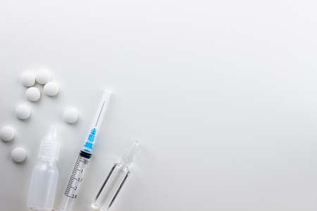 On a white background on the left are round white pills in bulk, drops, a syringe, an ampoule with medicine.の写真素材