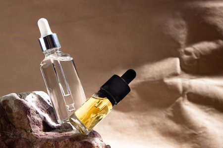 Two glass bottles with a pipette filled with transparent serum and yellow oil levitate on a beige...