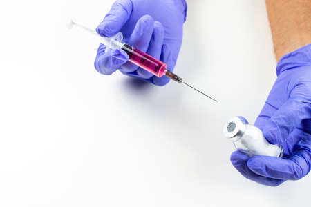 a disposable syringe with a needle and an ampoule with red (vitamin B12) liquid in male hands in blue (lilac) nitrile gloves. On a white background, lots of empty spaceの写真素材