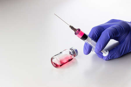 a disposable syringe with a needle and an ampoule with red (vitamin B12) liquid in male hands in blue (lilac) nitrile gloves. On a white background, lots of empty spaceの写真素材