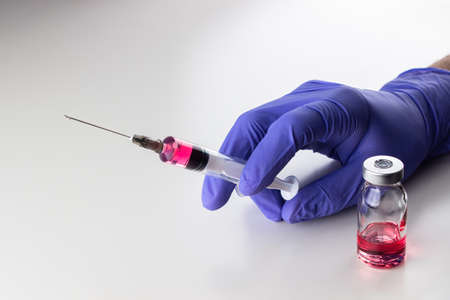 a disposable syringe with a needle and an ampoule with red (vitamin B12) liquid in male hands in blue (lilac) nitrile gloves. On a white background, lots of empty spaceの写真素材