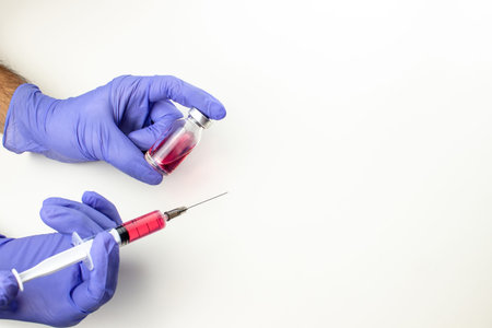 a disposable syringe with a needle and an ampoule with red (vitamin B12) liquid in male hands in...