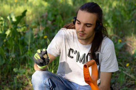 a young man holds a coin - garbage found using a wireless metal detector and a pinpointer in the park. grass in the backgroundの写真素材