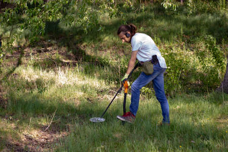 a young man in jeans, a black sweatshirt and wireless headphones is searching the ground in search of treasure using a pinpointer. nearby lies a wireless metal detector and a shovel stuck into the groの写真素材