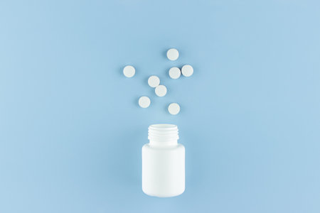 white round pills scattered from a white plastic jar on a blue backgroundの写真素材