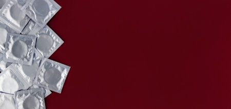 A lot of condoms in foil packaging lie on a dark red background, on the left side of the frame.  Lots of empty spaceの写真素材