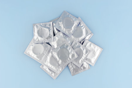A lot of condoms in foil packaging lie on a blue background, in the center of the frame. Safe sex and reproductive health concept.の写真素材