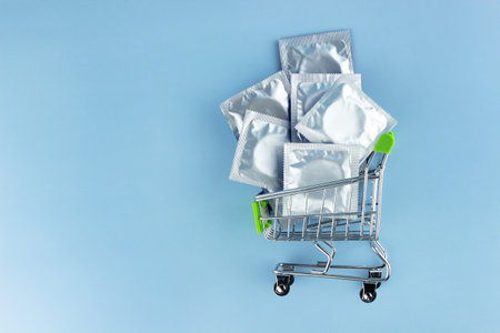 Many condoms in foil packaging in a shopping cart on a blue background. Safe sex and reproductive health concept.の写真素材