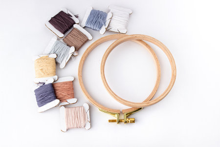 On a white background are cotton threads of different colors wound on bobbins and a round wooden hoopの写真素材