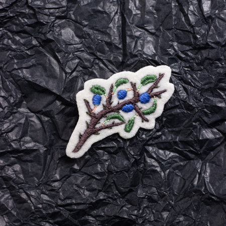 A brooch embroidered with threads on white felt in the form of a blackthorn. Against the background of crumpled black paperの写真素材
