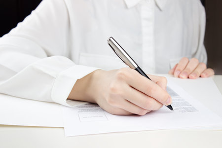Young woman filling out paperwork signing documents at a high counterの写真素材
