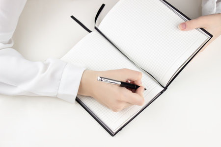 Young girl writes in a notebook, on a white table, top viewの写真素材