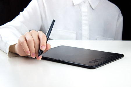 A young girl works on a wireless graphics tablet, holding a pen in one hand.の写真素材