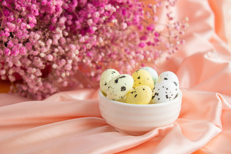 Easter composition on a background of pink satin quail eggs in a white ceramic bowl. On the back is a bouquet of pink gypsophilaの写真素材