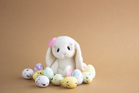 An Easter rabbit made of white chocolate sits among colored eggs on a beige background. Lots of empty spaceの写真素材