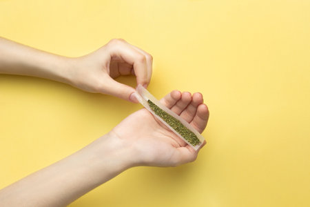 In female hands, paper for a joint, a filter and crushed medical marijuana. Against a bright banana yellow backgroundの写真素材