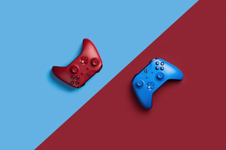 Two wireless gamepads red and blue lie on a background of opposite color. Confrontation of players, battle in the game onlineのeditorial素材