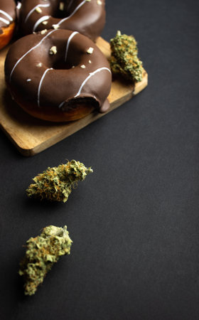 Dry buds of medical marijuana close-up with donuts covered with chocolate icing, sprinkled with nut crumbs. On a black backgroundの写真素材