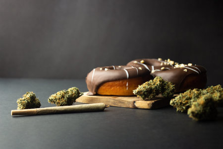 Chocolate-coated donuts lie on a black background next to medical marijuana buds and a joint. low...