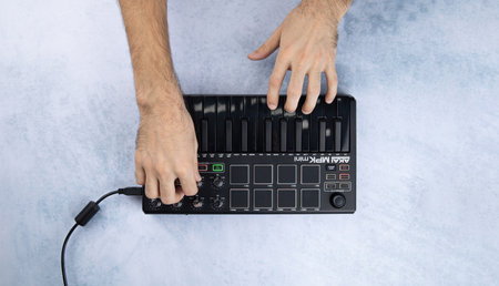 Male hands play the keys and rotate the encoder of the midi keyboard Akai mpk mini mk2 black, on a white and blue background. Top viewのeditorial素材