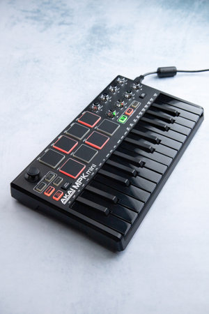 AKAI mpk mini mk2 black on a white-blue background, connected, buttons and pads light up. Side viewのeditorial素材
